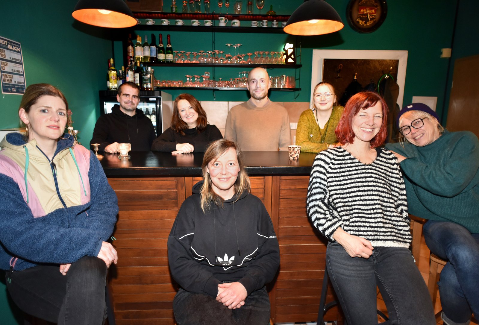 Eine Gruppe sitzt und steht um eine Bar herum und alle lächeln