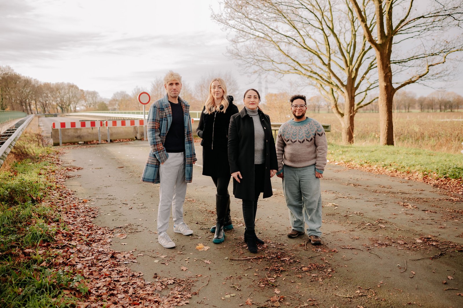 Vier Personen stehen auf einer Landstraße vor einer rot-weiß gestreiften Durchfahrtssperre