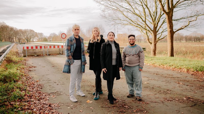 Vier Personen stehen auf einer Landstraße vor einer rot-weiß gestreiften Durchfahrtssperre