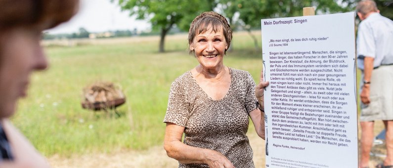 Auftraggeberin von Steinhöfel Regina Funke präsentiert ihr Dorfrezept auf einem großen Schild
