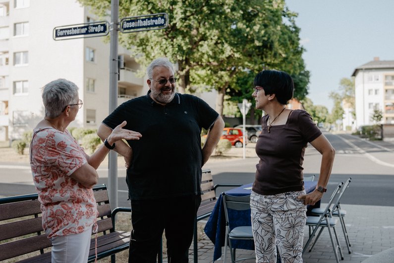 Three people are standing next to a street, talking.