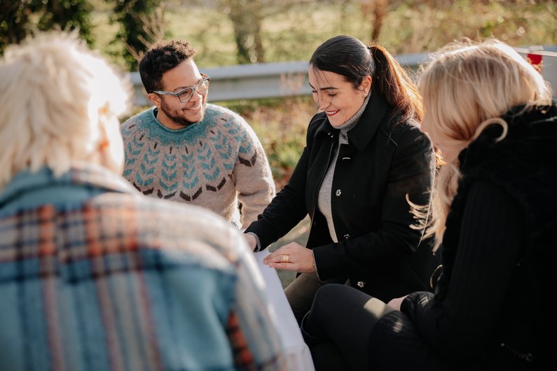 Vier Personen sitzen an einem Tisch im freien, vor einer abgesperrten Brücke