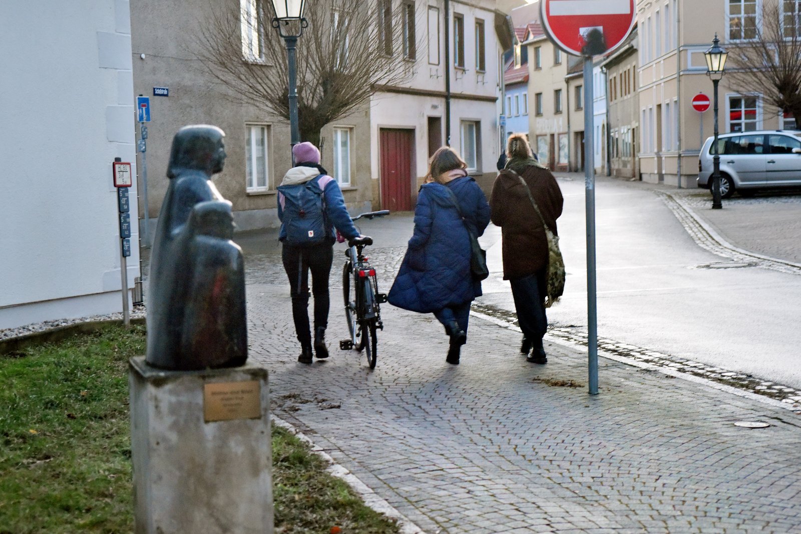 Drei Personen von hinten zu sehen mit Fahrrad, laufen bei Winterstimmung durch eine Dorfstraße
