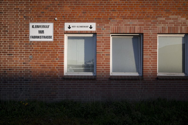 Backsteinwand mit Fenstern mit geschlossenen Rollläden und alten Schildern.
