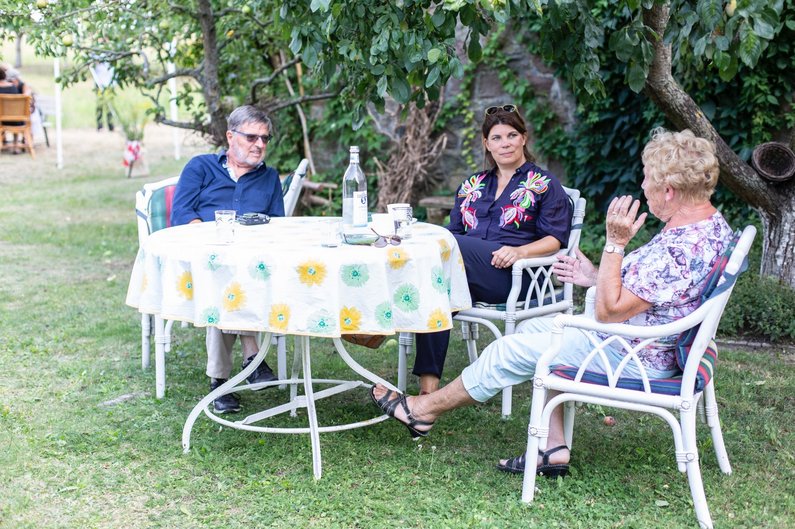Helgard Haug von Rimini Protokoll sitzt mit Auftraggebergruppe von Steinhöfel an einem Gartentisch