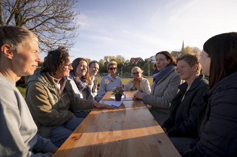 Eine Gruppe sitzt draußen an einem Tisch in der Abendsonne und unterhält sich.