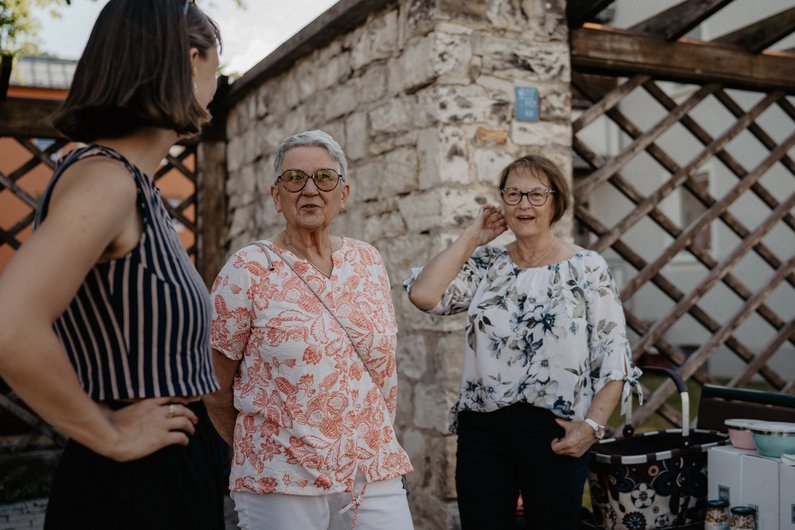 Three people are standing in front of a wall and talking.