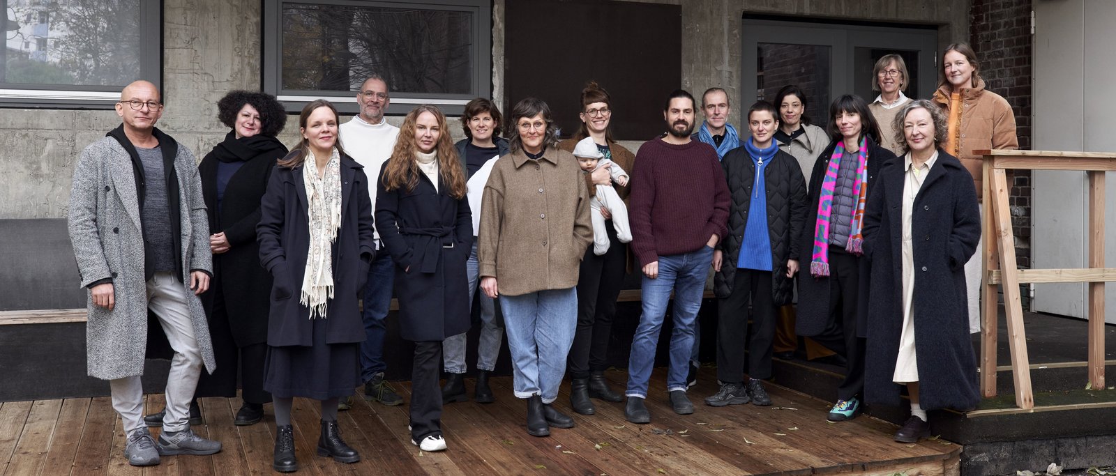 Group picture of 16 people on a wooden terrace in front of a building