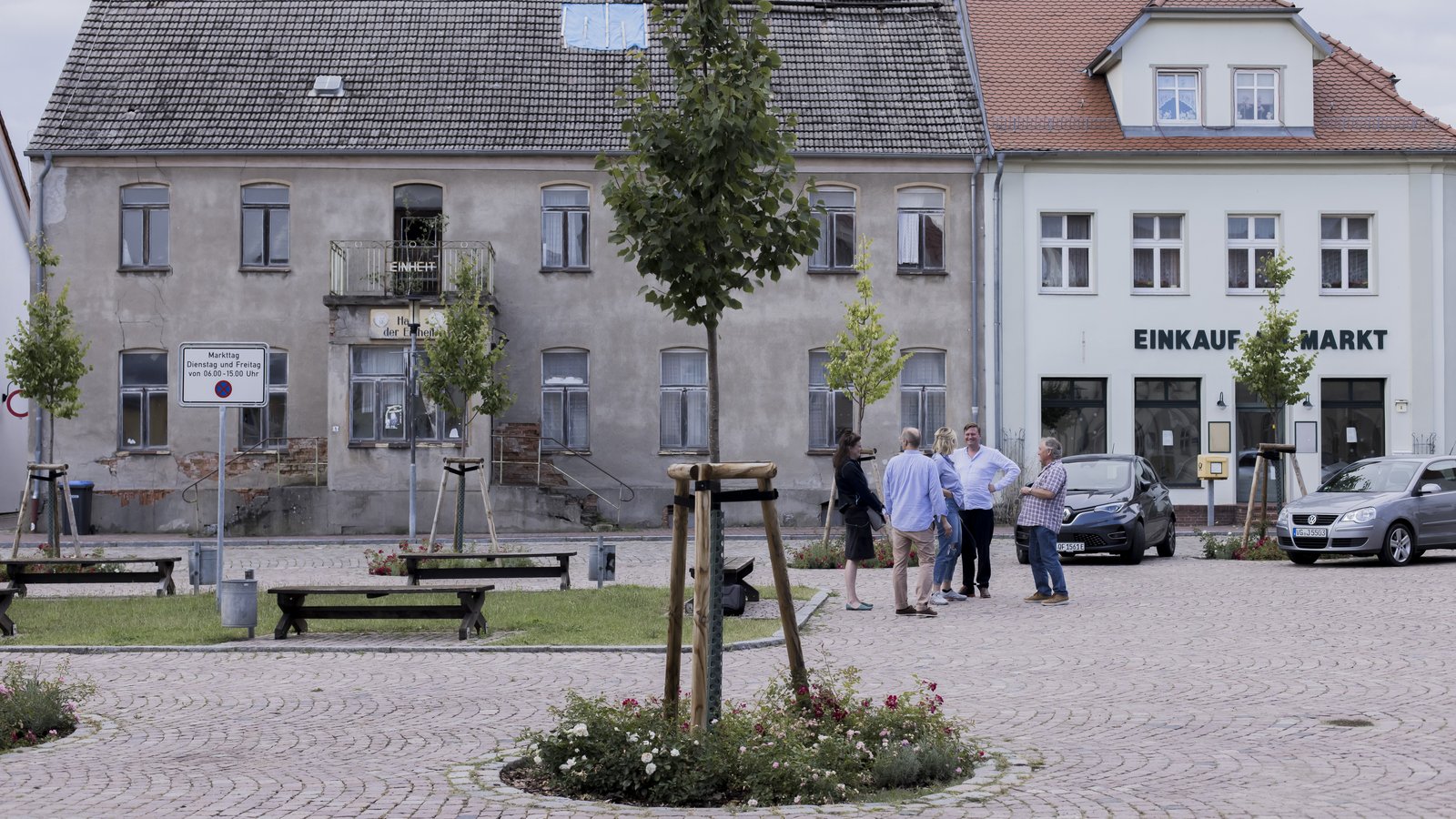 [Translate to English:] Personen der Neuen Auftraggeber, Häuser und Baum auf dem Marktpatz von Penkun