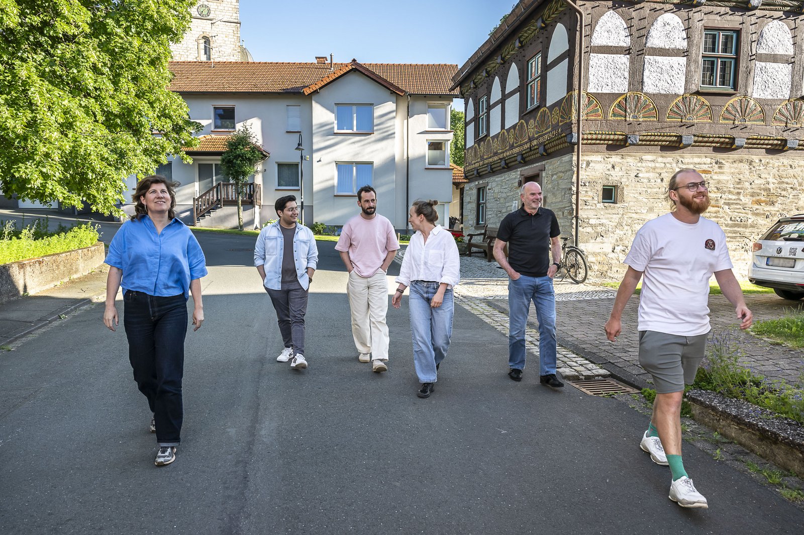 Six people are walking along a street with half-timbered houses.