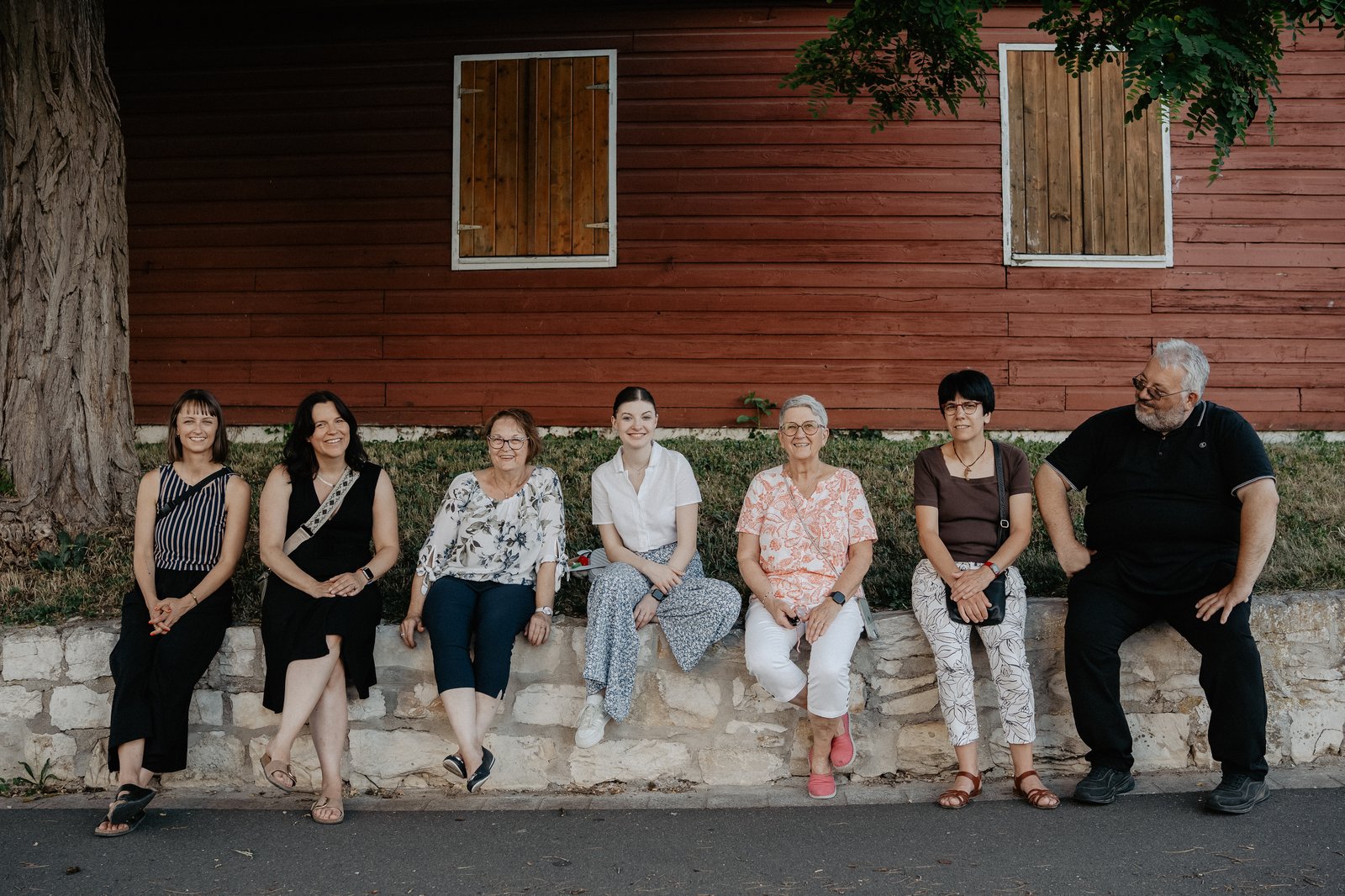 A group is sitting in a row on a small wall in front of a house.