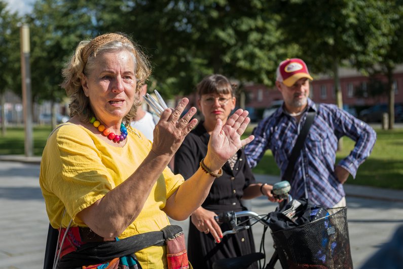 Three people are standing on a street, one of whom is articulating something with gestures.