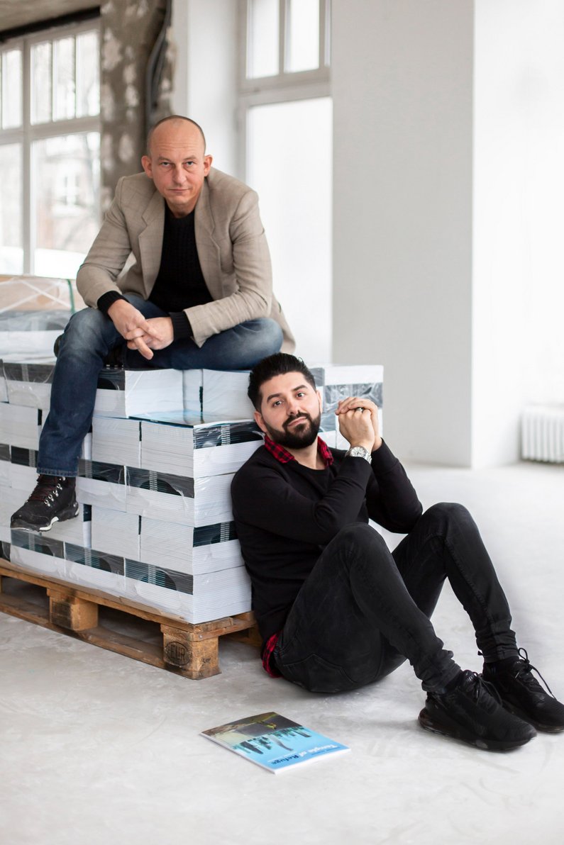 Mediator Alexander Koch und Auftraggeber von Berlin Sartep Namiq sitzen auf einer Palette der von ihm beauftragten Comicbücher Temple of Refuge 
