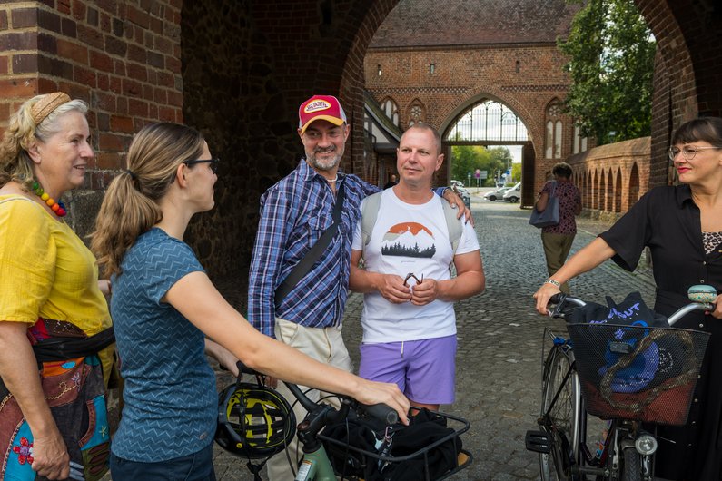 A group stands between brick buildings, talking.