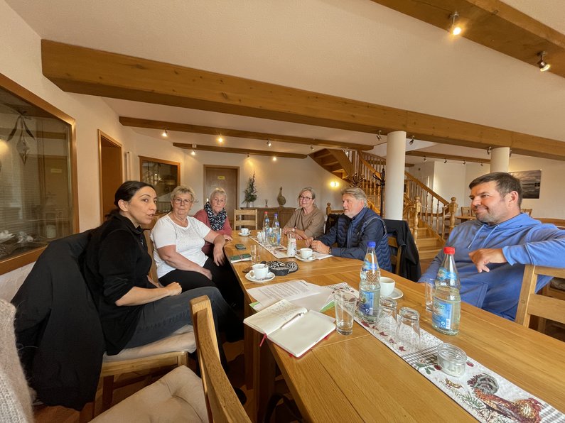 Several people are sitting around a large wooden table in a room.