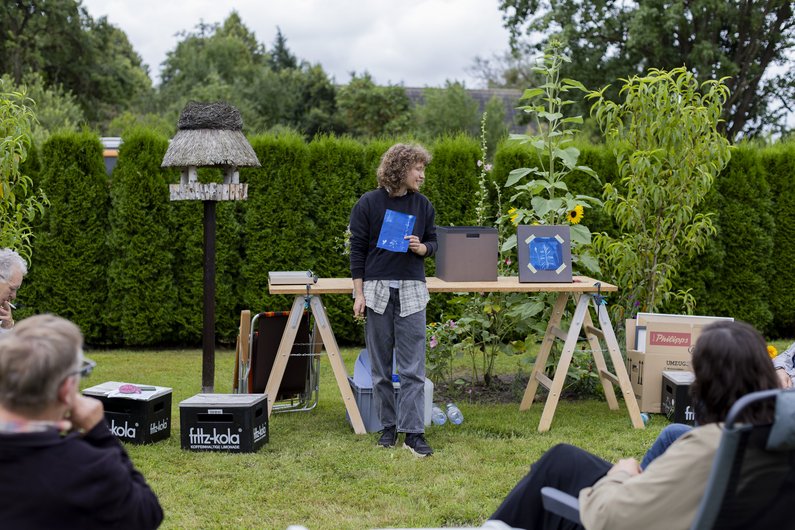 The New Patrons of Wietstock A person stands in front of a table in the garden and shows a picture.
