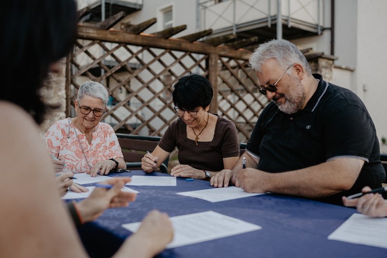 The New Patrons of Amberg – Am Bergsteig Four persons are sitting around a table in a garden, signing a paper