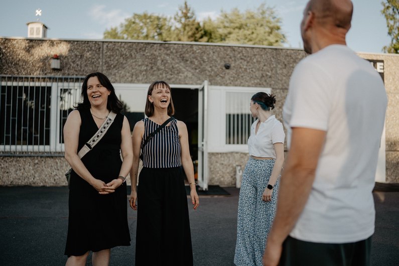 Three people are standing on a street, laughing, facing each other.