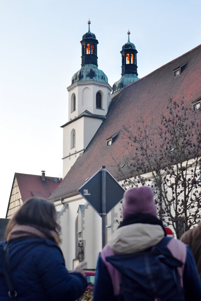 Ein Glockenturm, davor sind mehrere Personen von hinten zu sehen. 