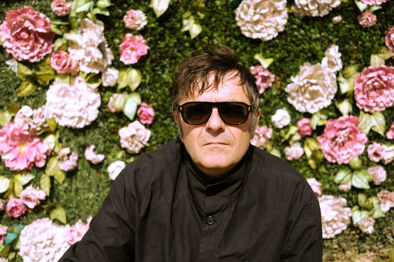 Eine frontale Aufnahme zeigt Künstler Christoph Schäfer mit Sonnenbrille vor einer Wand aus Rosenblüten in Kasnevitz