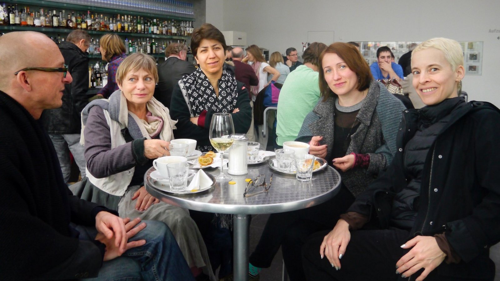 Künstlerin Candice Breitz mit Direktor der Neuen Auftraggeber Alexander Koch mit Neuen Auftraggeberinnnen sitzen in einem Café in Rostock