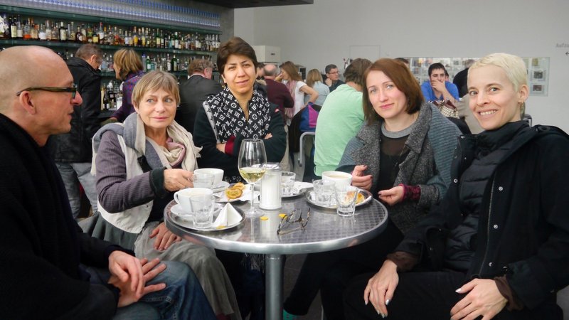 Künstlerin Candice Breitz mit Direktor der Neuen Auftraggeber Alexander Koch mit Neuen Auftraggeberinnnen sitzen in einem Café in Rostock
