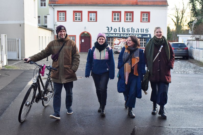 Vier Personen laufen bei herbstlicher Stimmung mit einem Fahrrad in einer Dorfstraße