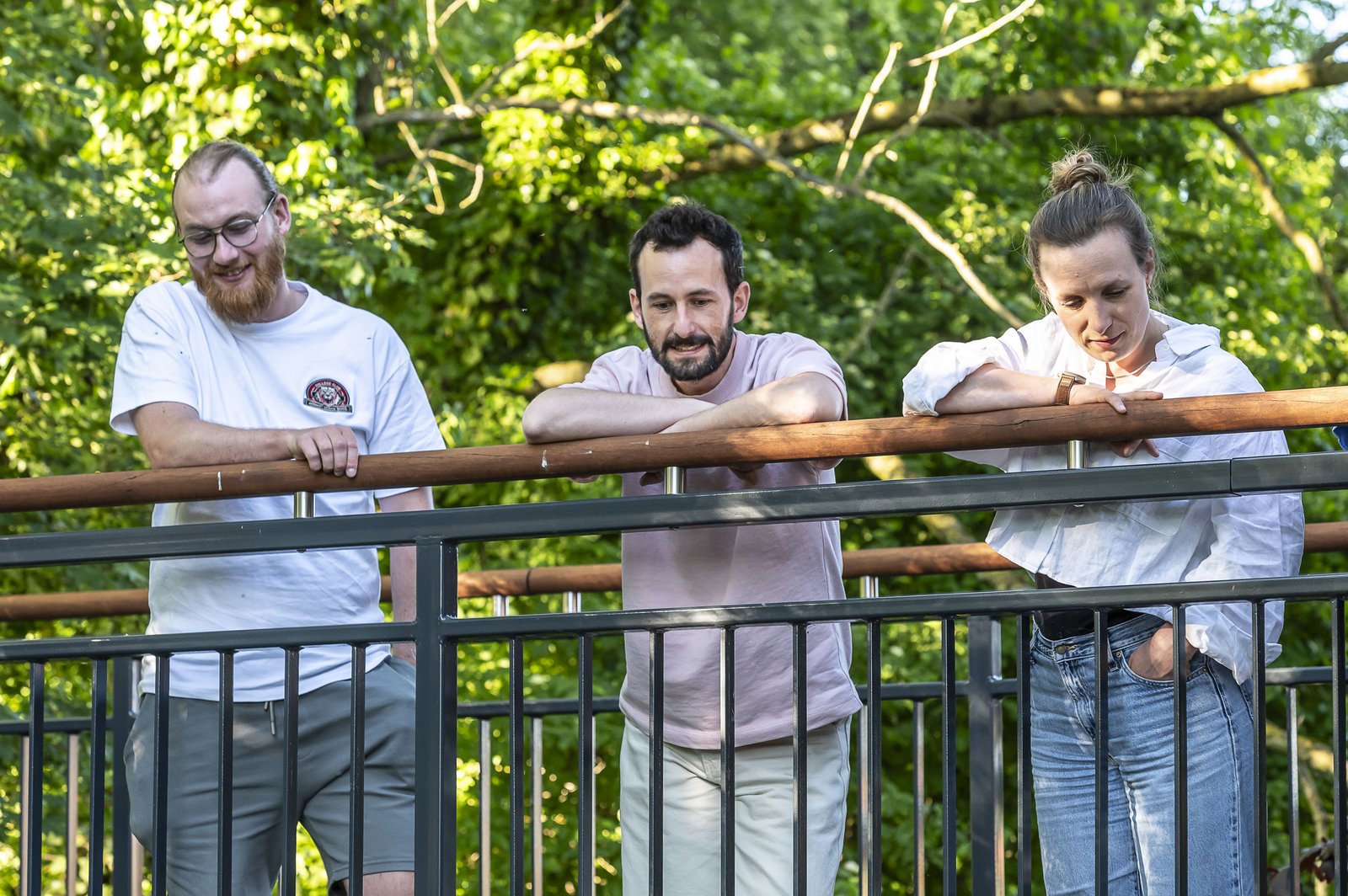 Three people standing on a bridge, looking down over the handrail.