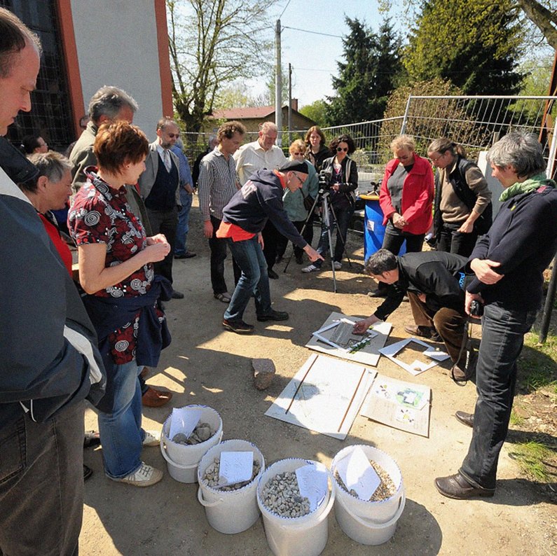 The group of new clients from Kleinliebenau stands in a circle and builds a model for the "Lustgang" with Atelier le balto using natural materials.