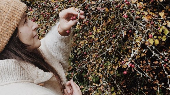 A person, Ruth Buchanan, in winter clothing stands in front of a bush and picks something