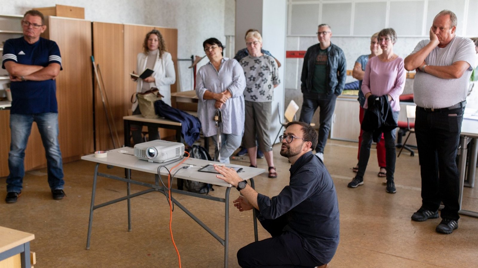 Members of The New Patrons of Züsedom standing around the artist Jakub Szczesny, who is presenting his ideas. 