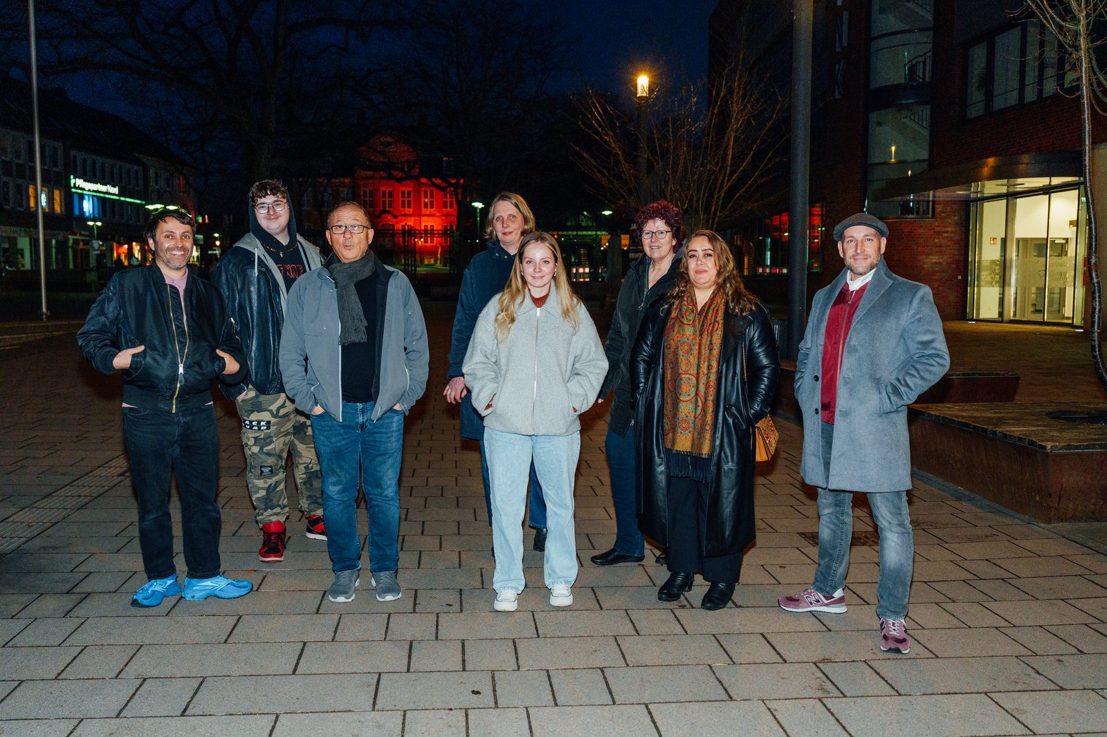 Die Neuen Auftraggeber von Pinneberg Eine Gruppe von Menschen steht für ein Foto zusammen auf einer Straße, es ist bereits dunkel.