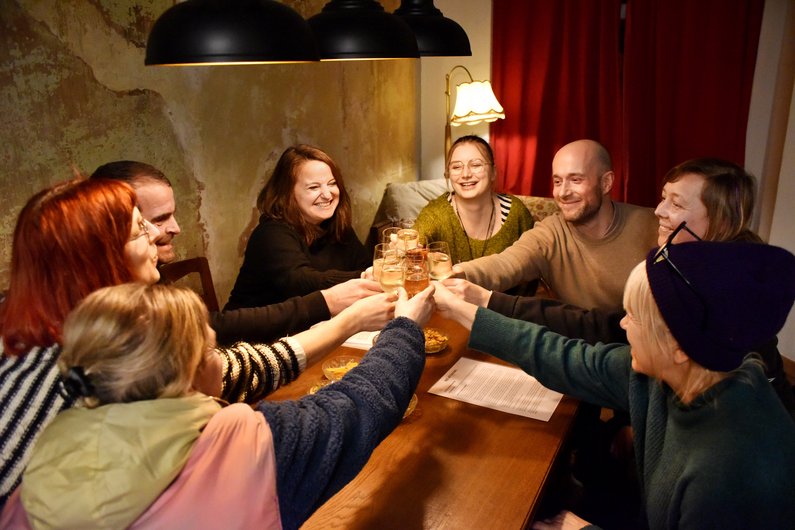 Mehrere Personen sitzen um einen Tisch und stoßen mit einem Getränk an