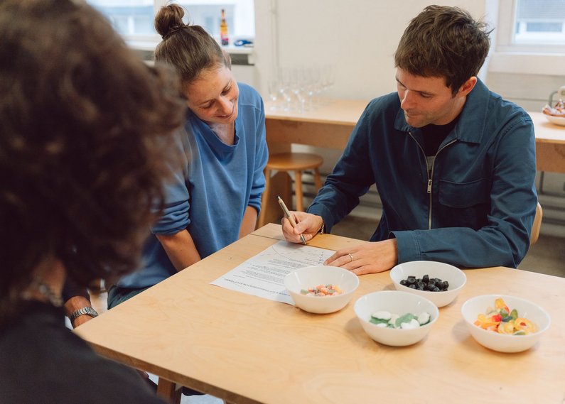 Three people are sitting around a wooden table and one person is signing a document