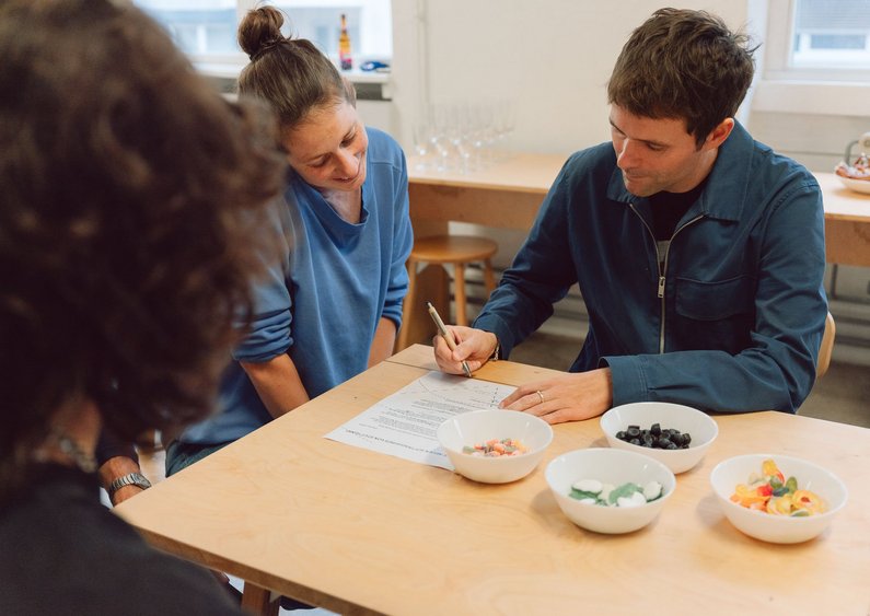 Drei Personen sitzen um einen Holztische und eine Person unterzeichnet ein Papier