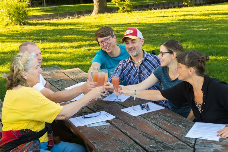 The New Patrons of Neubrandenburg Six people are sitting around a table on a lawn and clinking glasses.