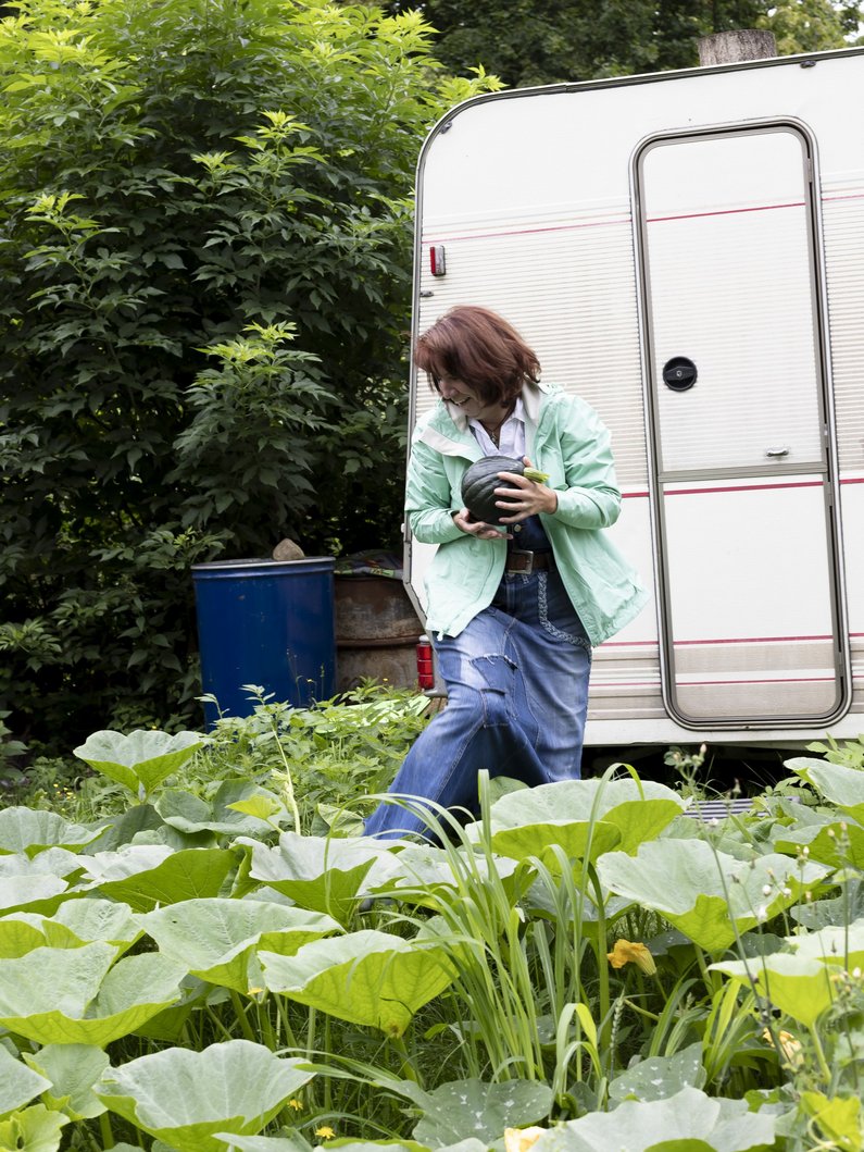 Die Neuen Auftraggeber von Wietstock Eine Person steht im Garten vor einem Wohnwagen
