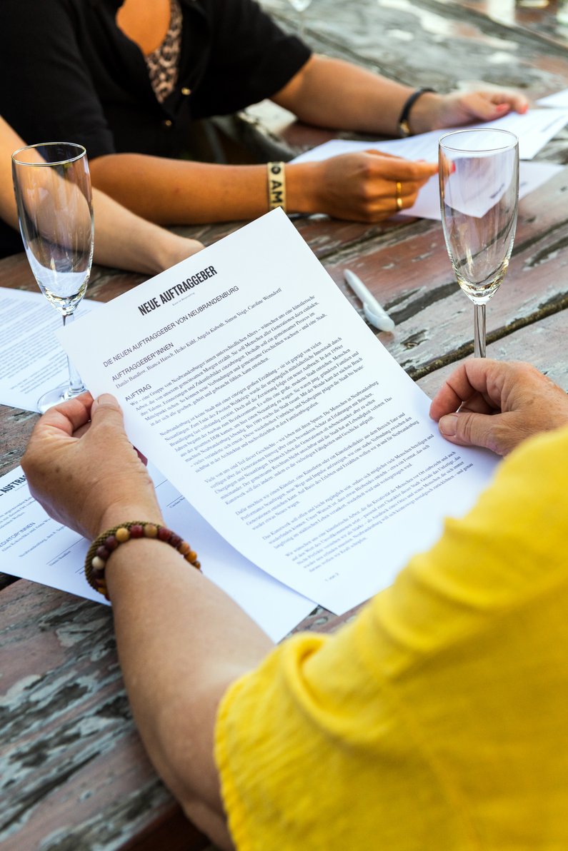 The New Patrons of Neubrandenburg Hands holding a document, next to it a champagne glass