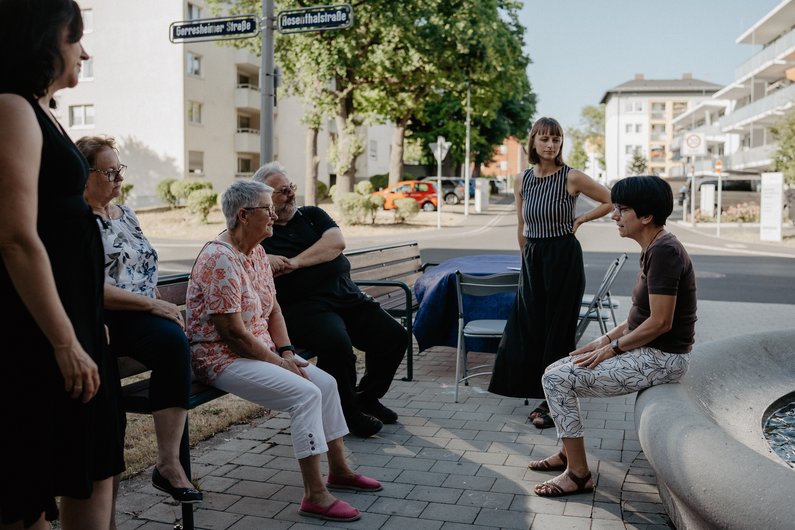 Several people are standing and sitting on a street, facing each other.